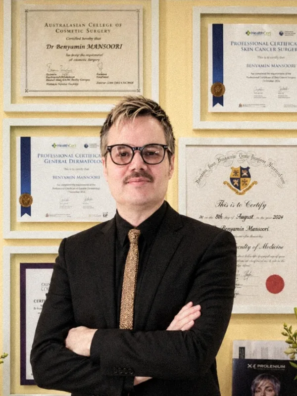 Dr Benyamin Mansoori standing in front of his framed medical qualifications and certificates